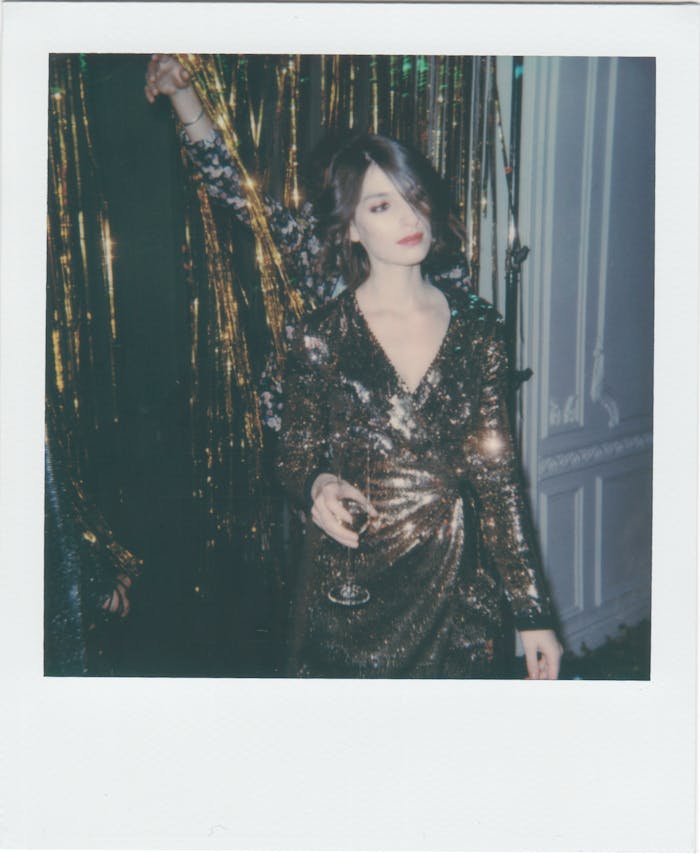 Stylish woman in a gold dress holding a wine glass at a festive indoor party.